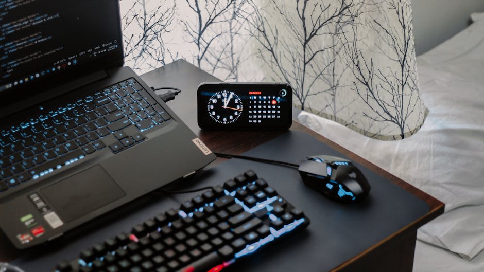 A modern workspace featuring a laptop, digital clock, gaming mouse, and keyboard, ideal for work and tech enthusiasts.